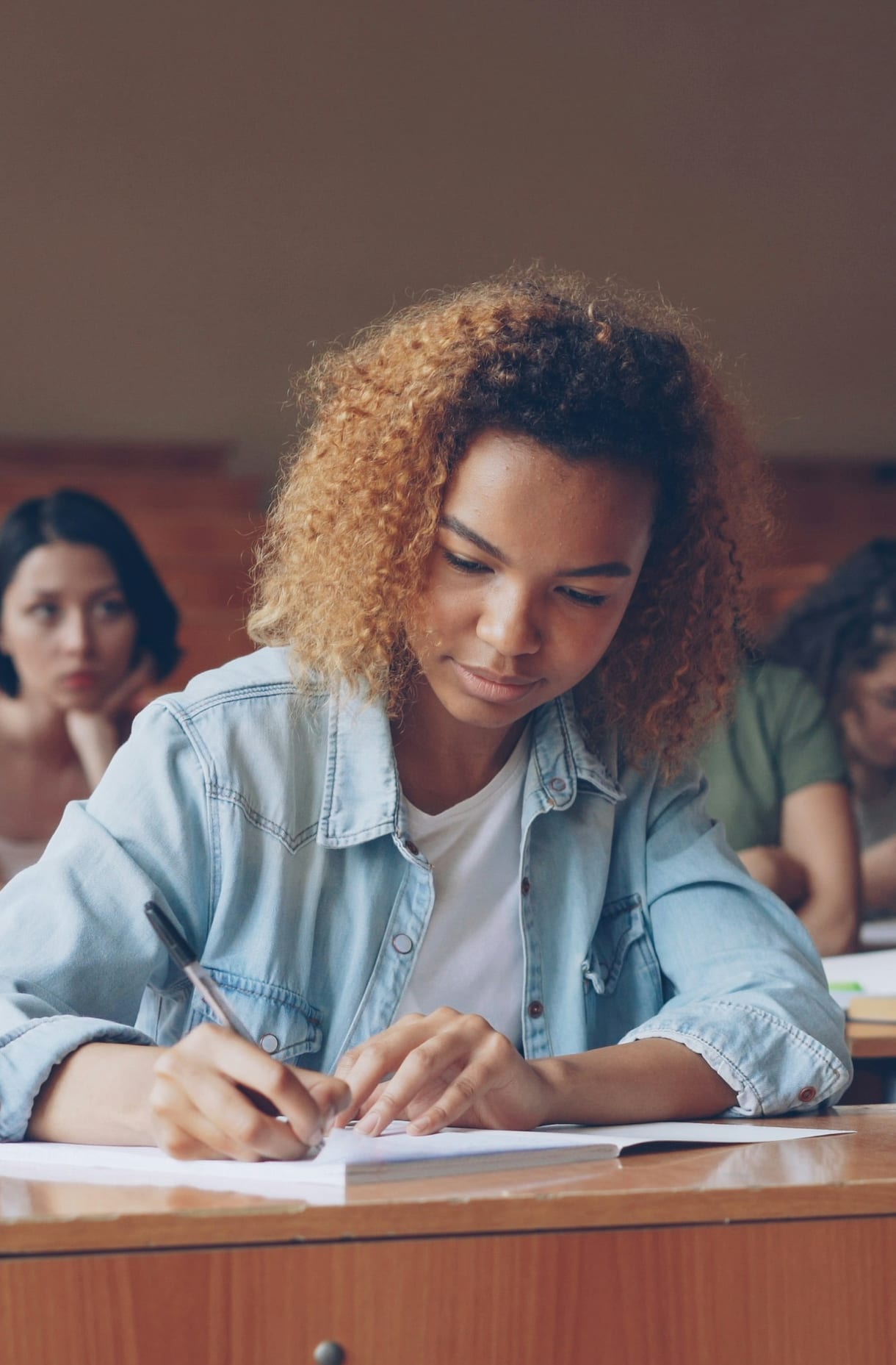A student writing notes at a desk in a lecture hall